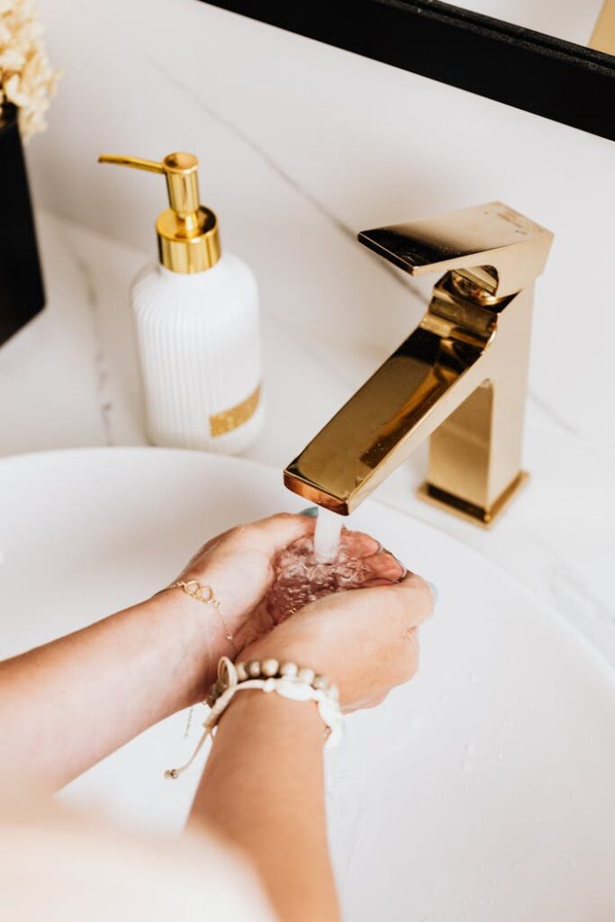 Elevated view of hands washing under a gold faucet in a modern bathroom, promoting cleanliness and hygiene.