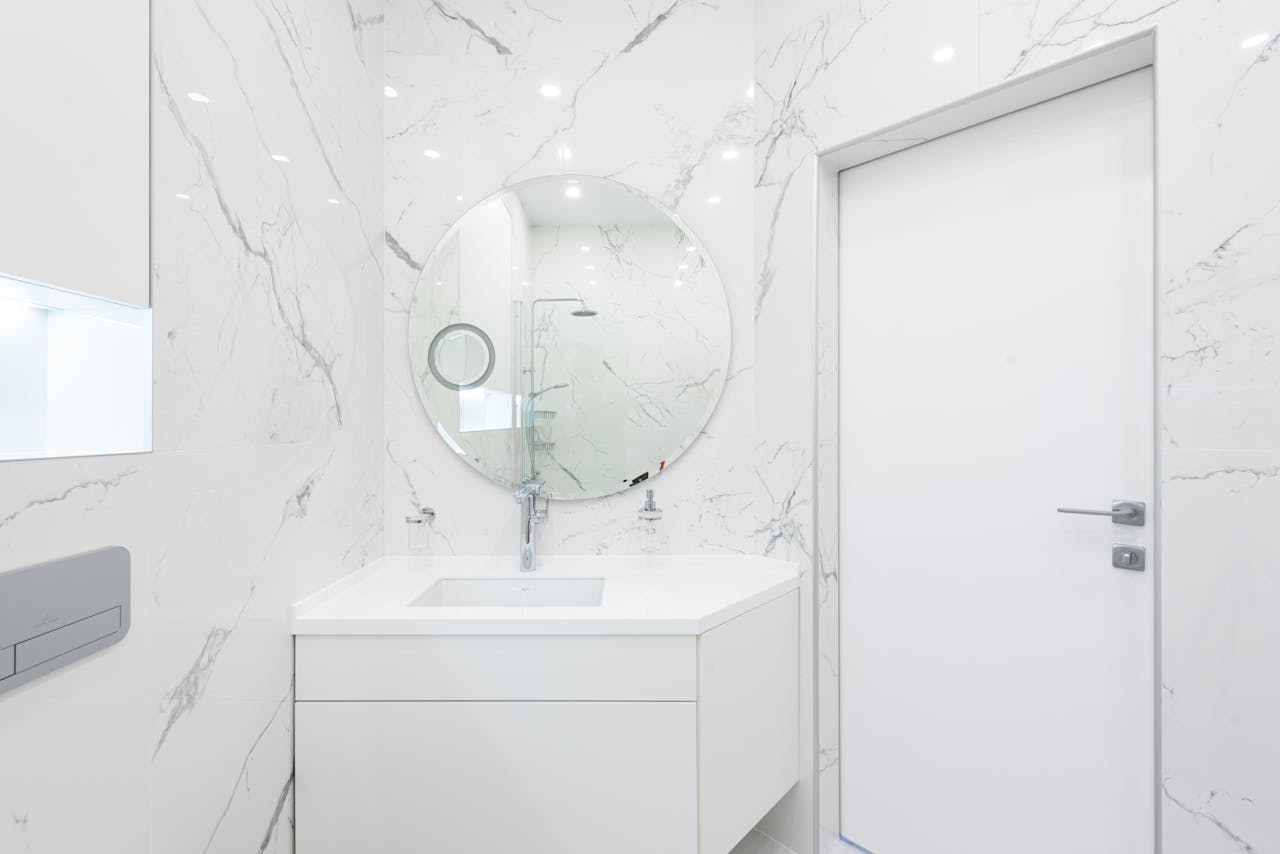 Elegant white marble bathroom with modern design and reflective mirror, emphasizing minimalism.